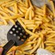 Closeup of stirring and turning over frying french fries with spatula. Fast food, healthy nutrition, cooking in oven.